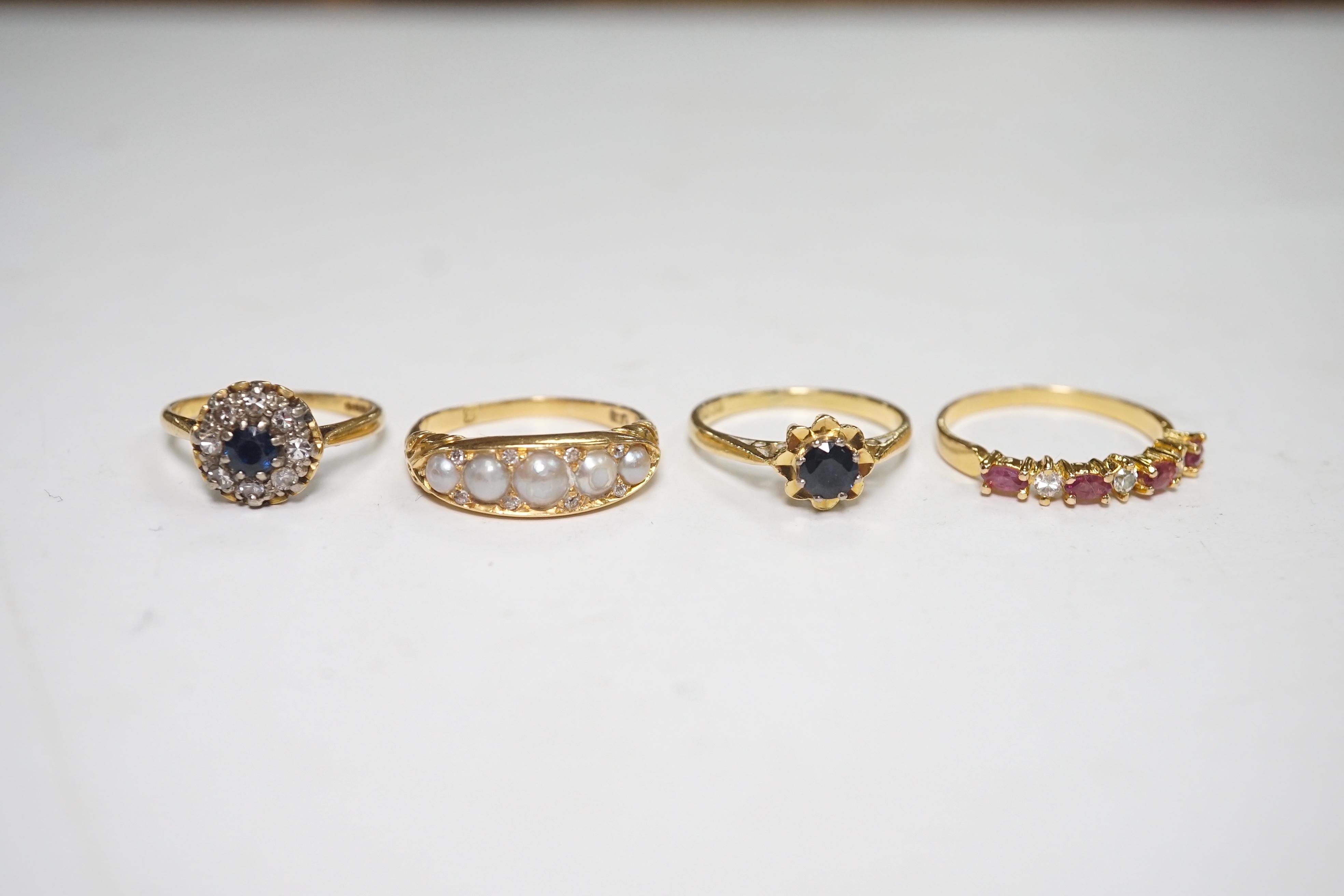 A late Victorian yellow metal and five stone split pearl set half hoop ring, with diamond chip spacers, size N/O, two modern 18ct gold and gem set rings and one other ring. Condition - fair to good
